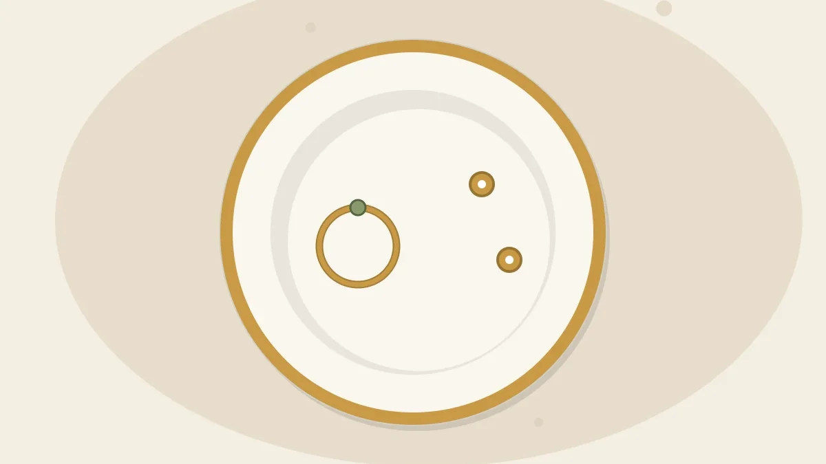 A small white clay jewelry dish with a mustard-gold painted rim holding a ring and a pair of small stud earrings, seen from above