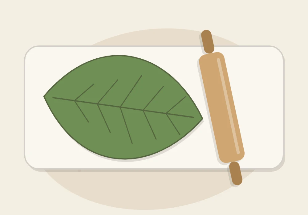 A green leaf lying vein-side down on a clay slab with a rolling pin pressing over it