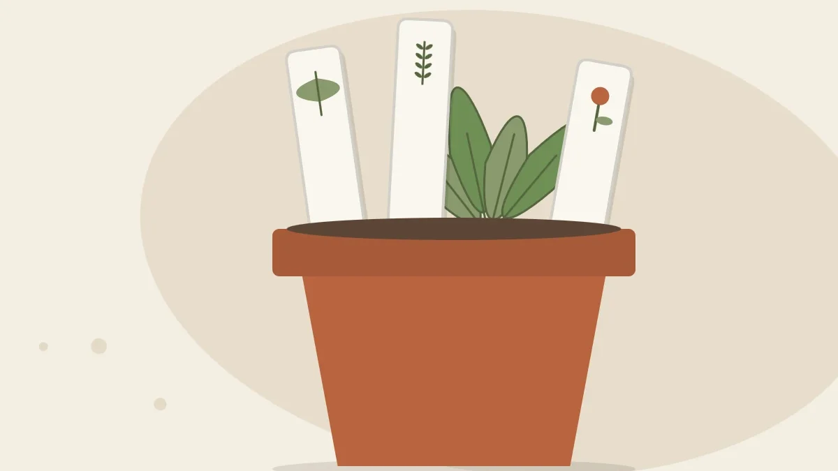 Three clay plant markers with painted leaf symbols standing in a terracotta pot with a small green plant