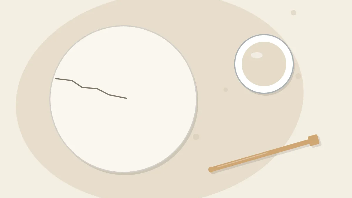 A round clay disc with a thin hairline crack running in from the edge, beside a small pot of clay slip and a wooden tool