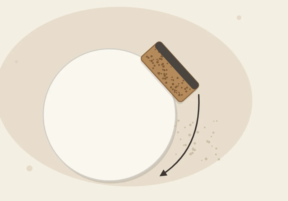 A sanding block moving along the edge of a clay disc with an arrow showing the direction and fine dust specks beside it